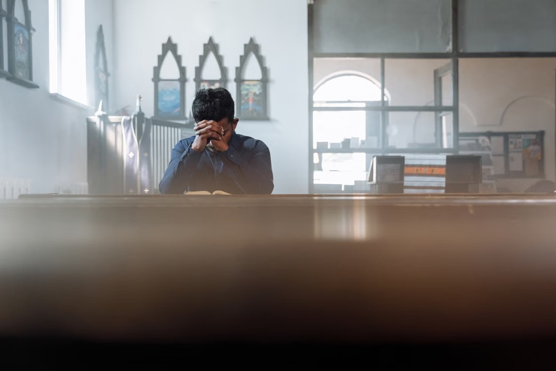 An image of a person praying in a church with their hands together