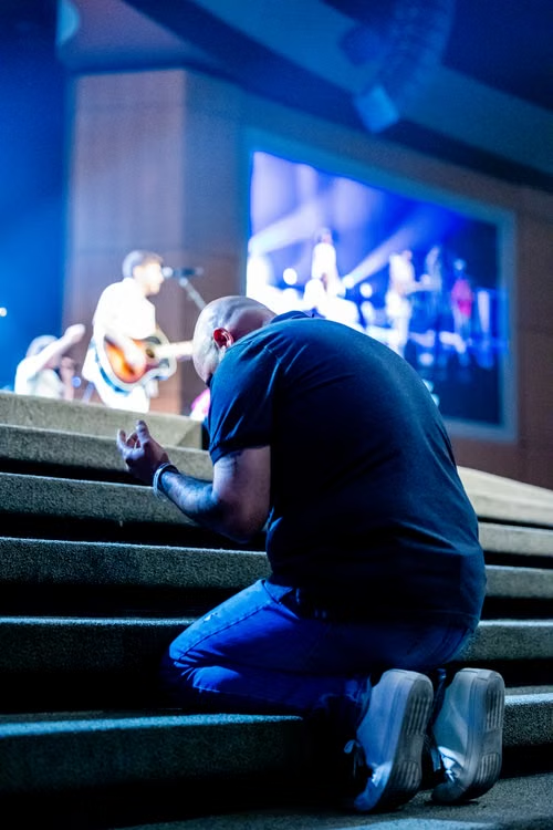 An image of a person praying in a church with a live band