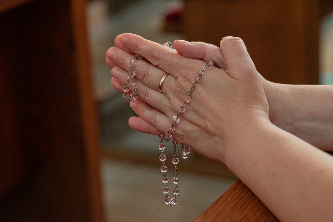 An image of a person praying with their hands together, holding a rosary